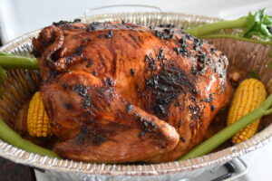 An oven tray with a roasted turkey featuring some dark spots, decorated with four cellery sticks and two corncobs.