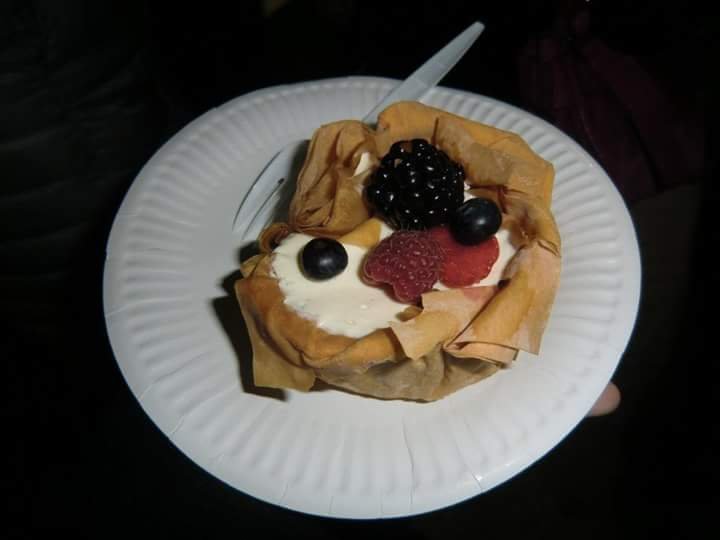 A white paper plate with a parcel cheesecake in the middle. It looks like a bowl-shaped crepe with a white creamy filling and berries on top.
