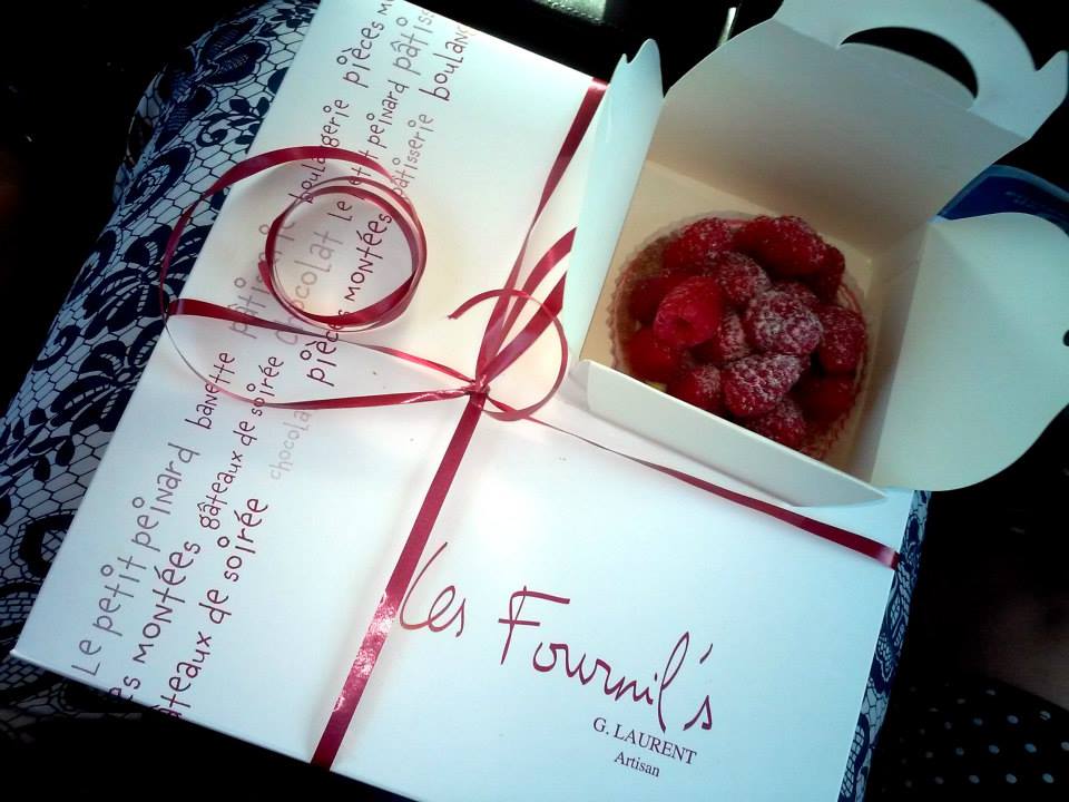 A white pastry box with a read bow and the logo of the bakery Les Fournil's, Artisan G. Laurent.