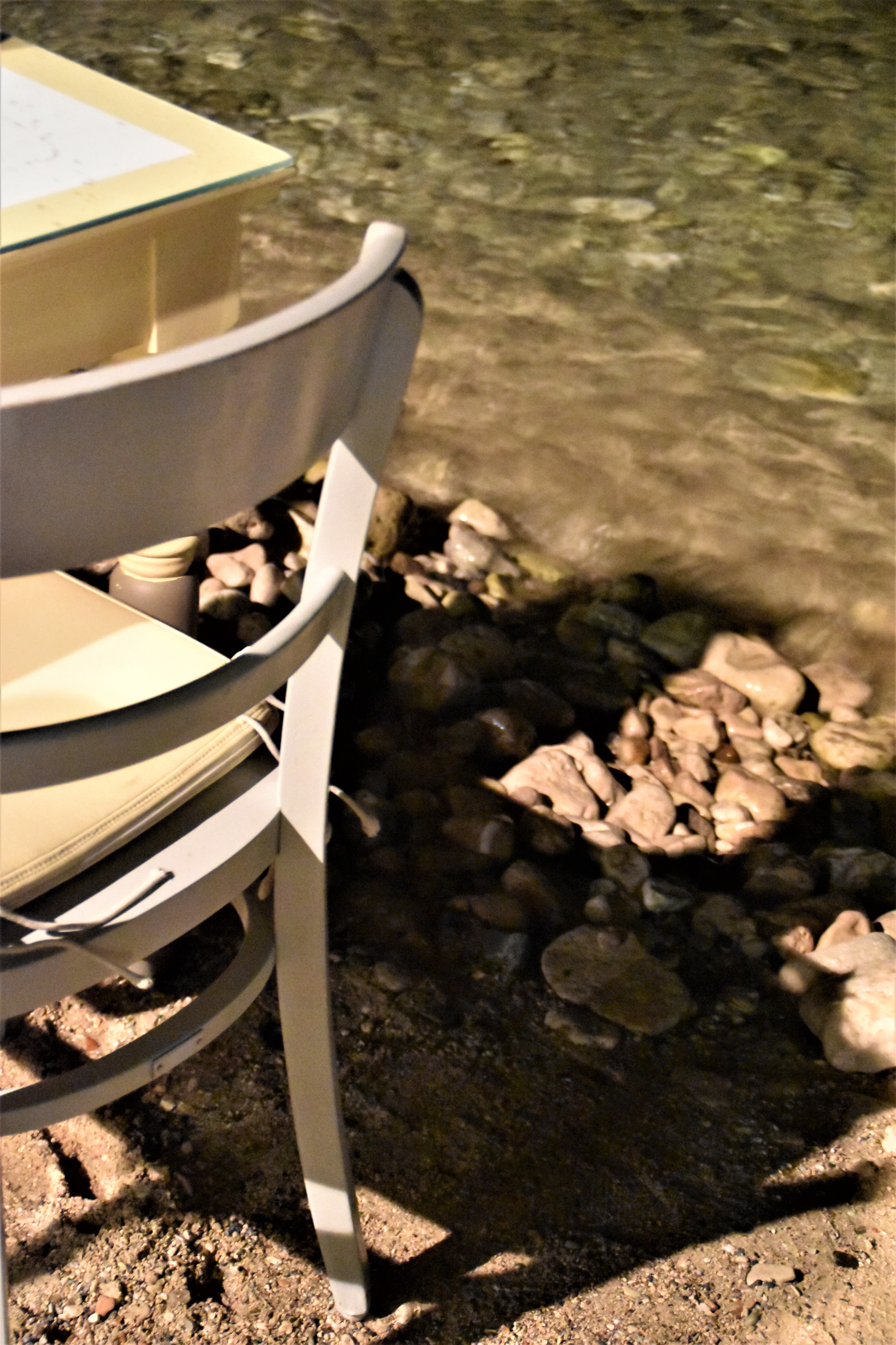 A close-up of a white chair right by the shore, where turquoise waters almost touch its legs.