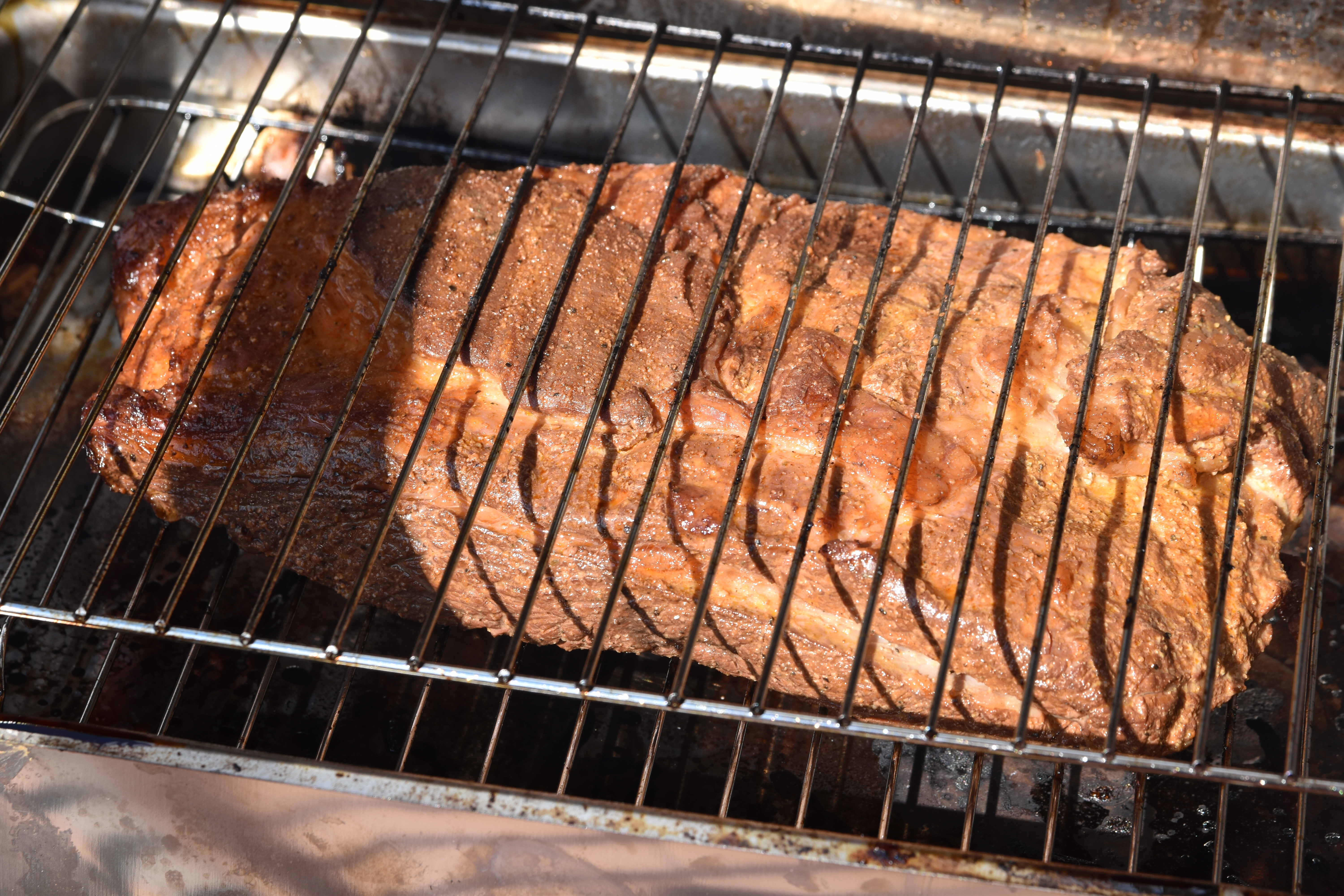 Two pounds of brownish brisket on a smoker's rack.