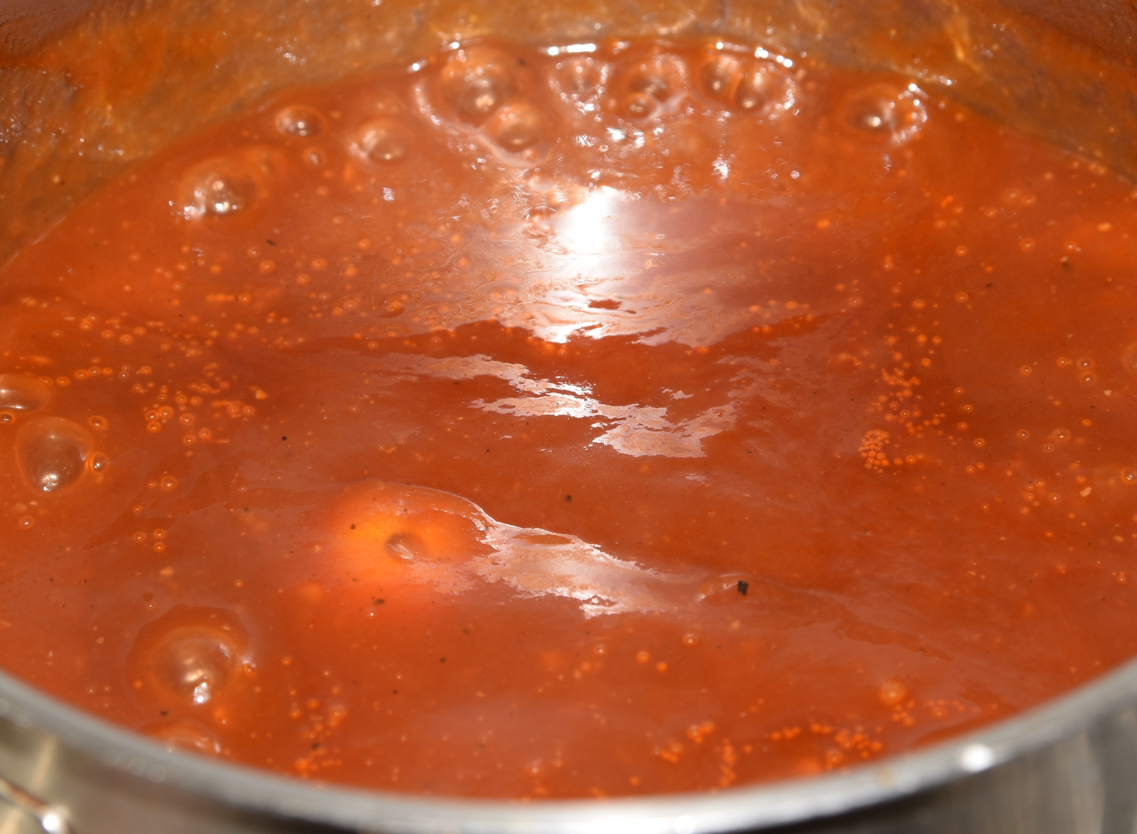 A close-up of a simmering intense red sauce, where a tomato is shyly floating.